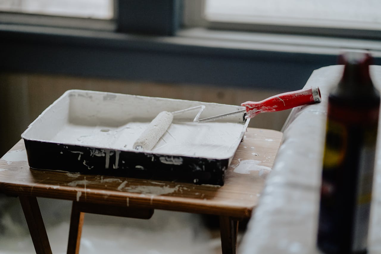 A paint roller and tray with white paint on a wooden table, indicating a renovation work.